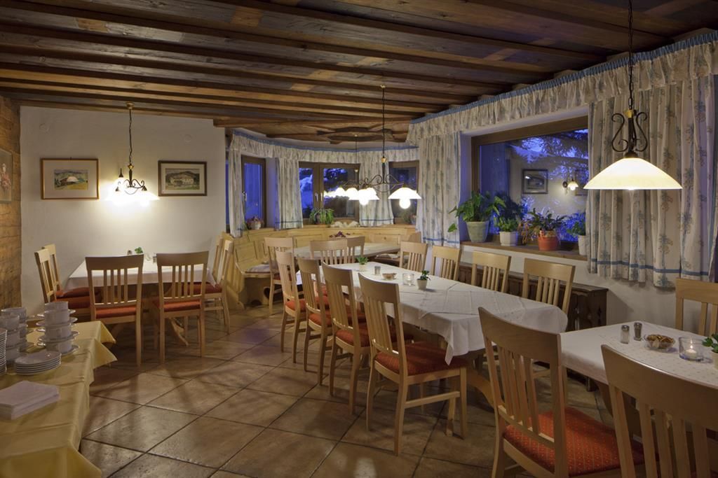 A cozy restaurant with wooden furniture and soft lighting. The tables are set, and there are small plants by the window.